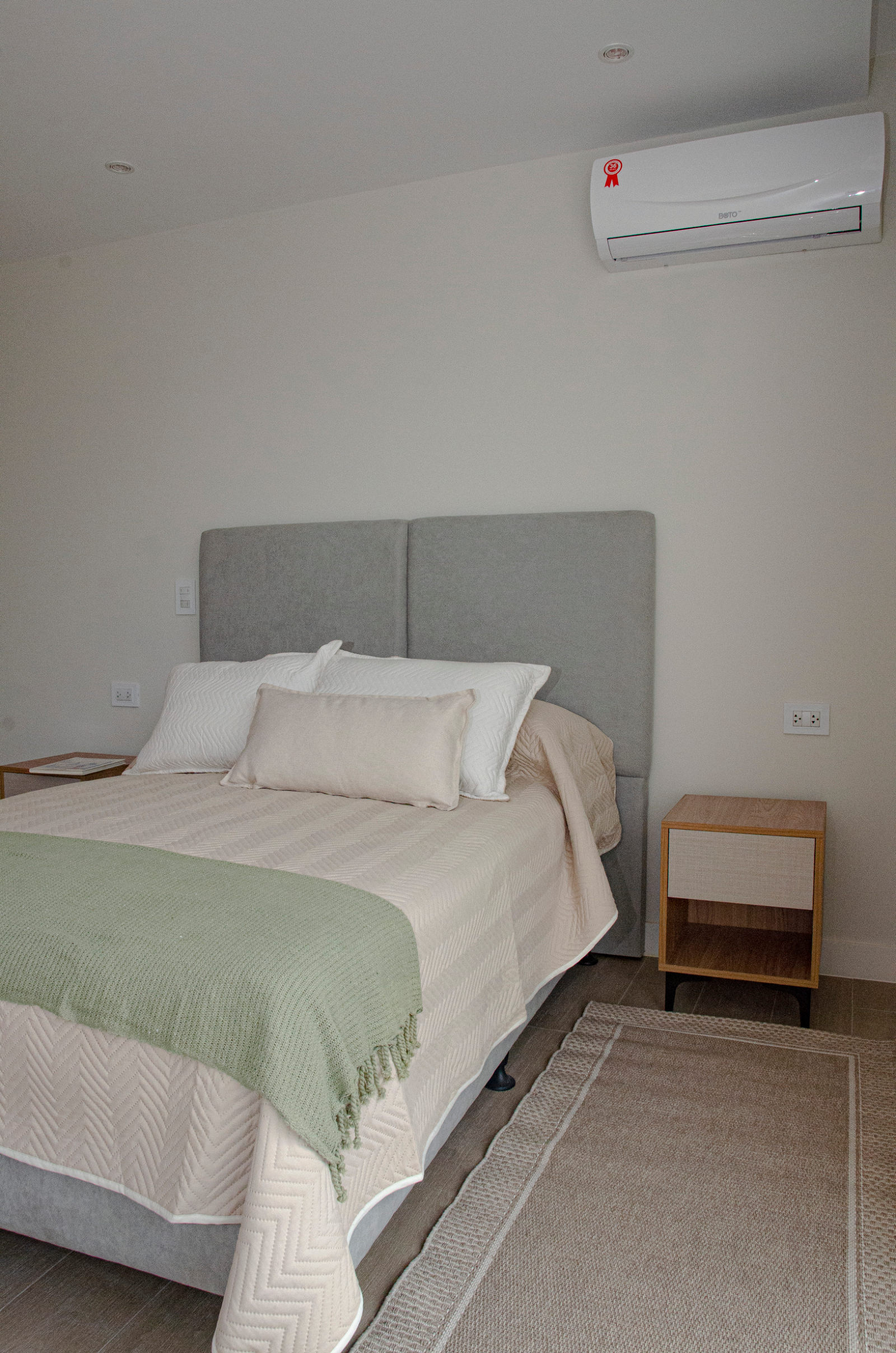 Dormitorio principal del departamento modelo, con aire acondicionado y mesa de luz